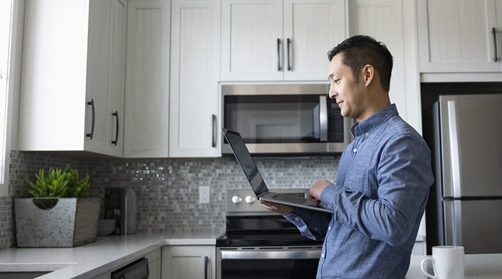 A business owner standing in their kitchen while using their laptop to review a business proposal