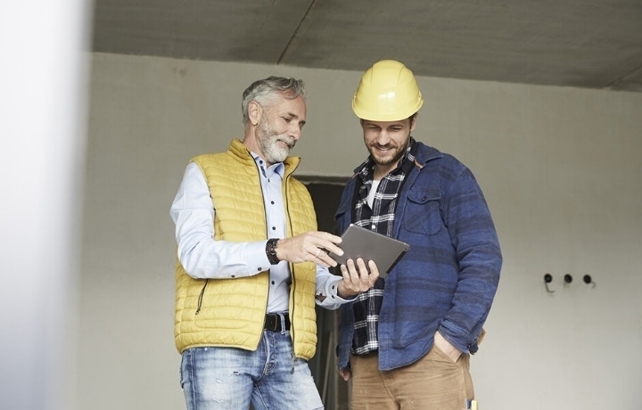 A photo of two people looking at a tablet while standing inside a room at a construction site.