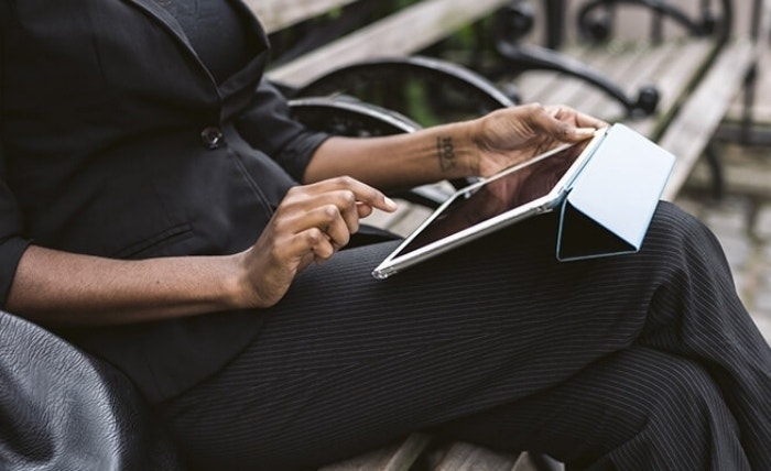 An image of a person sitting at a park bench and using a tablet on their lap.